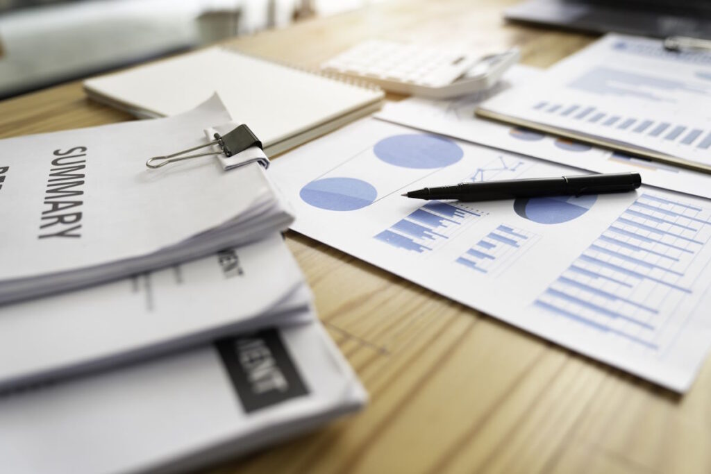 Paper report. Blue graphs and charts. Business reports and a pile of documents on a wood table background.
